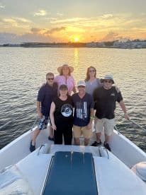 A cheerful group gathers on the bow of a boat, enjoying a stunning sunset — perfect for memorable celebrations on the water.