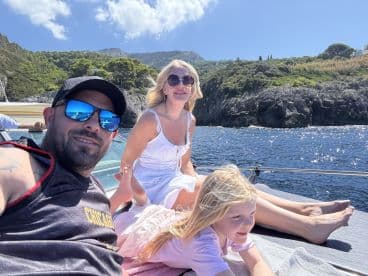 A joyful family enjoys a sunny day on the boat, capturing precious moments against a stunning coastal backdrop.