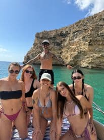 A lively group of friends poses for a fun photo on a boat against a stunning coastal backdrop, perfect for beach outings and celebrations.