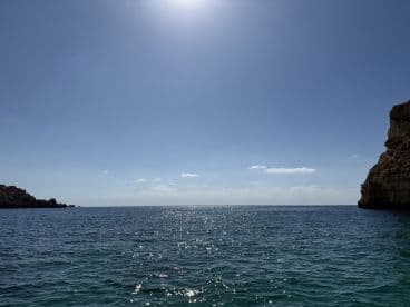 A scenic view of the ocean with rocky cliffs in the background, showcasing a clear sky and shimmering water.
