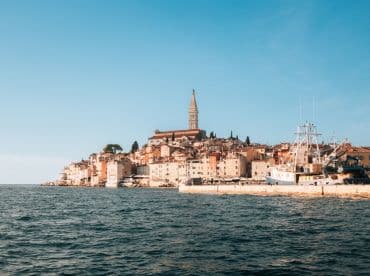 A picturesque view of a charming coastal town with colorful buildings and a historic tower, showcasing the beauty of the harbor and surrounding waters.