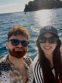 A cheerful couple enjoys a sunny day on the water, capturing a memorable selfie with sparkling waves in the background.