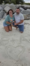 A couple poses on the beach, playfully showcasing their initials in the sand — a perfect moment for romantic beach getaways or proposals.