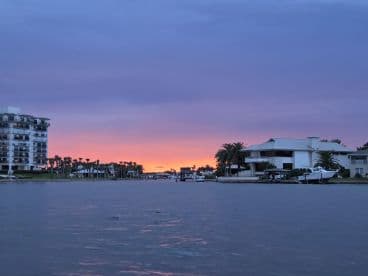 A stunning sunset paints the sky over a tranquil waterfront scene, showcasing beautiful homes along the coastline — perfect for evening boat cruises.