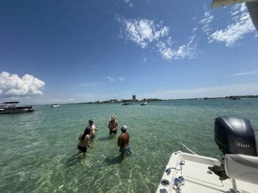 A lively group enjoys a sandbar stop, wading in the clear waters while surrounded by boats — a perfect day for fun and relaxation on the water.