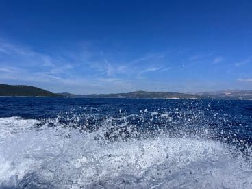 A dynamic shot capturing the ocean's splash as the boat speeds through the water, showcasing the vibrant blue sky and scenic coastline in the background.