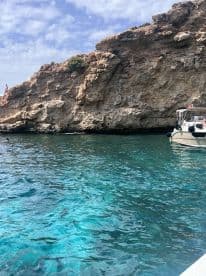 A stunning view of a rocky coastline with a boat anchored nearby, while a person enjoys the crystal-clear waters — a perfect snapshot of a day on the water.