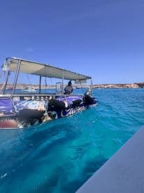 A boat operator navigates through crystal-clear waters, showcasing the vibrant scenery of the coastline — perfect for exploring the beauty of the sea.