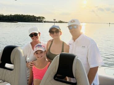A joyful family poses for a photo on their boat during a beautiful sunset, capturing a memorable moment on the water.