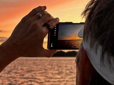 A person captures a stunning sunset over the water with their smartphone, showcasing the beauty of the moment during a boating experience.
