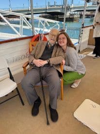 A joyful moment captured aboard a boat, featuring a young woman smiling with an elderly man, showcasing the warmth of family connections and celebrations on the water.