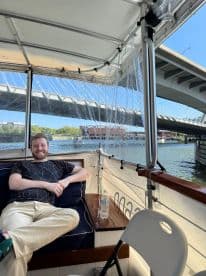 A relaxed moment inside a boat cabin, featuring a comfortable seating area and a scenic view of the water and bridge. Perfect for enjoying a leisurely day on the water.