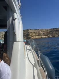 A side view of a boat cruising along a rocky coastline, showcasing the vessel's structure against a clear blue sky.