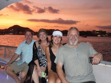 A cheerful group enjoys a sunset cruise, capturing a memorable moment against a stunning backdrop of vibrant colors on the water.