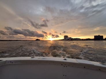 A stunning sunset view from the bow of a boat, showcasing the tranquil waters and distant skyline — perfect for evening cruises.
