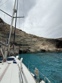 A stunning view of a sailboat anchored near rocky cliffs, surrounded by vibrant turquoise waters — perfect for exploring secluded coves.