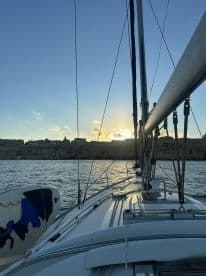 A serene view from the deck of a sailboat at sunset, showcasing the vessel's structure and the picturesque backdrop of the coastline.
