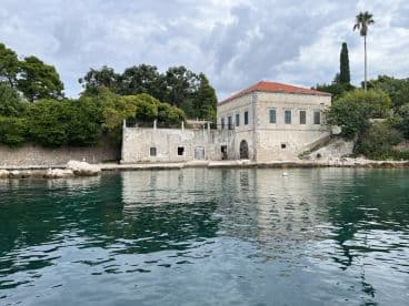 A serene view of a historic building along the coastline, surrounded by lush greenery and calm waters, perfect for capturing the beauty of island destinations.