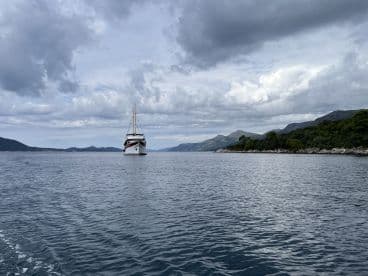 A majestic yacht navigates through calm waters, framed by a stunning mountainous coastline under a dramatic sky — perfect for luxury cruising experiences.