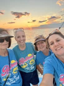 A group of friends celebrating retirement enjoy a sunset cruise, capturing joyful moments against a stunning backdrop of the setting sun over the water.
