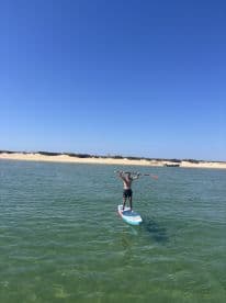 A person joyfully paddleboards in clear waters, showcasing an exciting on-water activity against a beautiful beach backdrop.