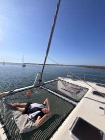 A guest relaxes on the netting of a catamaran, enjoying the sunshine and tranquil waters — a perfect moment for leisure on the open sea.
