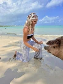 A woman interacts with a friendly pig on the beach, creating a memorable wildlife experience in the Bahamas — a unique encounter with nature.