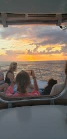 Guests enjoy a stunning sunset view from the deck of a boat, capturing the moment with their phones — a perfect setting for memorable celebrations on the water.