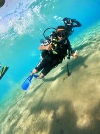 A young diver gives a thumbs up while exploring underwater, showcasing the excitement of diving adventures in crystal-clear waters.