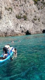 A group enjoys a fun day of paddleboarding and swimming in crystal-clear waters near a rocky coastline, perfect for adventure seekers and nature lovers.