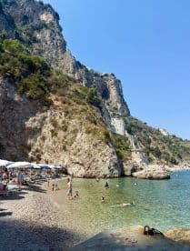 A vibrant beach scene with groups of people swimming and sunbathing along a stunning coastline, perfect for a relaxing day by the water.