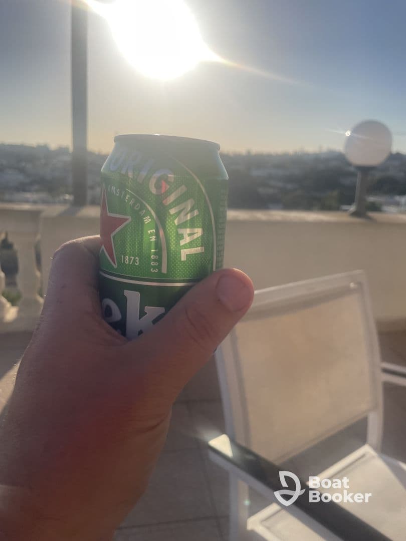 A hand holding a can of beer against a bright sun backdrop, suggesting a relaxed atmosphere, possibly on a boat or outdoor setting.