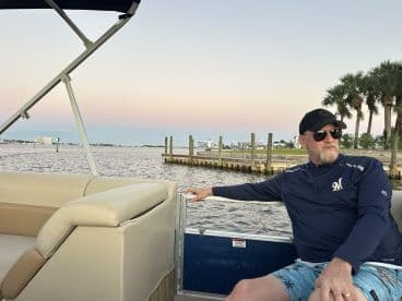 A man relaxes on a boat, enjoying the scenic waterfront view during sunset — a perfect moment for leisure and exploration on the water.