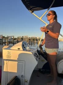 A woman stands at the helm of a boat, engaged in conversation while enjoying a beautiful day on the water. The interior setup showcases the boat's console and seating area.