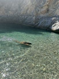 A swimmer enjoys the crystal-clear waters of a secluded cove, surrounded by stunning rocky cliffs — a perfect spot for a refreshing dip during a boating adventure.