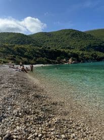 A vibrant beach scene with people enjoying the clear waters and pebbled shore, perfect for a relaxing day under the sun.