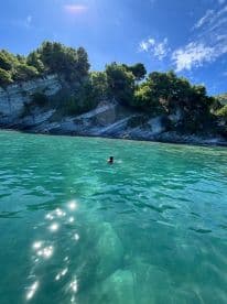 A swimmer enjoys the crystal-clear waters near a scenic rocky coastline, perfect for a refreshing dip during a boating adventure.