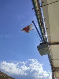 An unclear view of a flag and part of a boat structure against a blue sky, lacking a clear focus on the main subject.