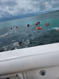 A lively group enjoys swimming in the clear waters, wearing life jackets for safety — a perfect day for water activities and family fun.