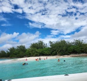 A lively scene at a beautiful beach with groups of people enjoying swimming and relaxing in the turquoise waters — a perfect sandbar stop for family fun.
