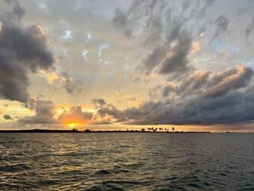 A breathtaking sunset over the coastline, with rays of light breaking through the clouds, creating a picturesque scene perfect for evening cruises.