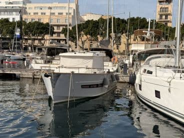 A sleek yacht docked in a marina, showcasing its elegant design against a backdrop of other vessels and waterfront buildings.