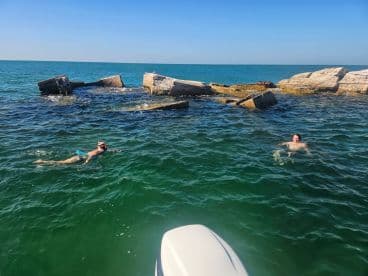 Two swimmers enjoy a snorkeling adventure near rocky formations in clear waters, showcasing the beauty of marine exploration.