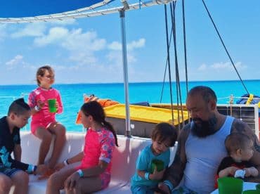 A joyful family enjoys drinks on a boat, surrounded by stunning ocean views — perfect for a fun day out on the water with kids.