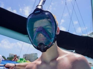 A young adult prepares for snorkeling with a full-face mask, showcasing the excitement of underwater exploration during a boating adventure.