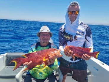 Two anglers proudly display their impressive catch while fishing on a boat in the open ocean — a perfect moment for fishing enthusiasts.