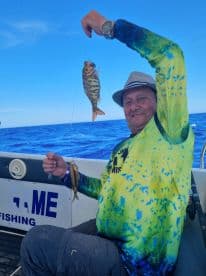 A man proudly displays his catch while fishing on a boat in the open ocean, showcasing the thrill of deep-sea fishing adventures.