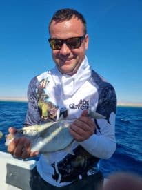 A happy angler proudly displays his catch while fishing in the ocean, showcasing the thrill of a successful day on the water.
