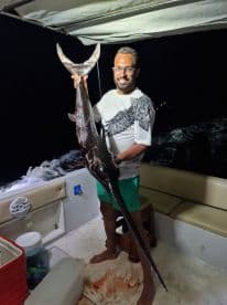 A proud angler displays his impressive catch during a night fishing adventure, showcasing the thrill of deep-sea fishing experiences.