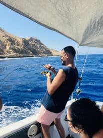 A man enjoys fishing on a boat, showcasing the thrill of on-water activities against a stunning coastal backdrop.